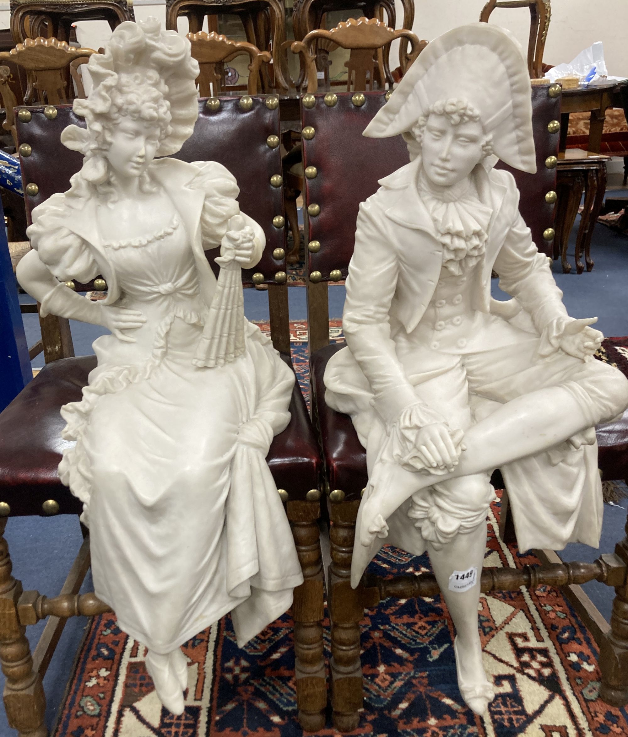 A pair of resin marble seated figures of a Dandy and a Dandizette on ebonised plinths